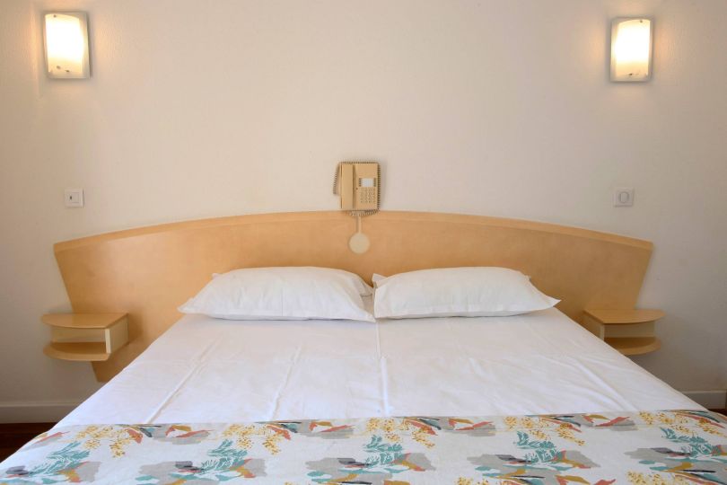 Classique Une chambre simple avec un lit, deux oreillers, un téléphone mural et des étagères de chaque côté.