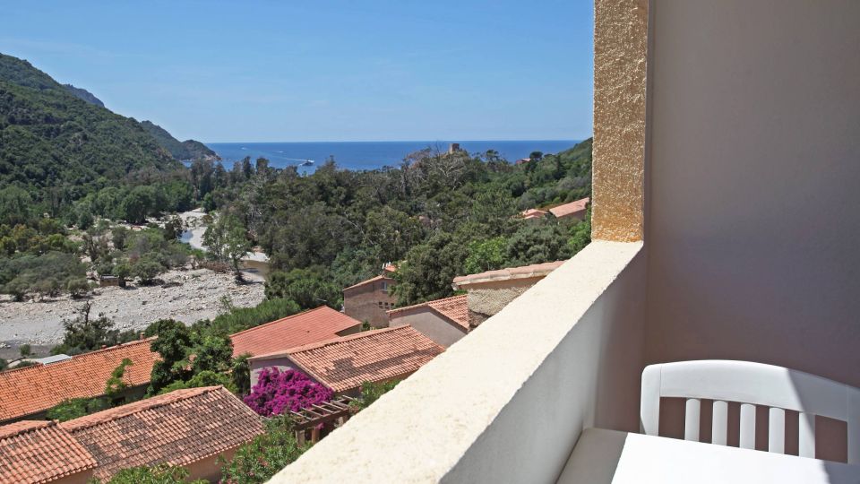 Confort Une vue calme depuis un balcon, avec des maisons, des montagnes et la mer au loin sous un ciel bleu.
