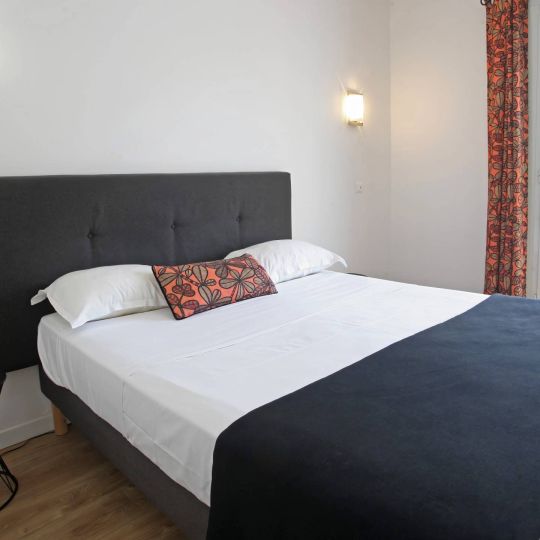 Confort Chambre moderne avec un grand lit, décor simple et vue sur l'extérieur à travers une porte-fenêtre.