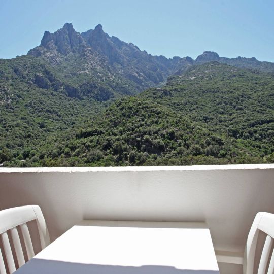 Confort Une vue magnifique des montagnes verdoyantes depuis un balcon avec une table et des chaises blanches.