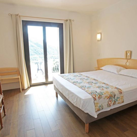 Classique Chambre lumineuse avec lit double, bureau, fauteuil, et balcon donnant sur la nature. Télévision murale incluse.