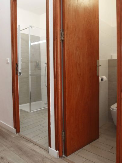 Confort Une salle de bain moderne avec douche et WC, vue à travers des portes en bois. Sol en carrelage clair.