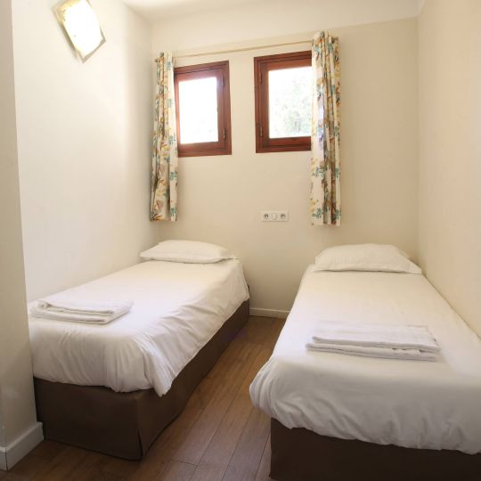 Classique Chambre simple avec deux lits séparés, murs clairs et fenêtres laissant entrer la lumière. Ambiance calme et lumineuse.